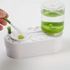 A hand is using a brush to clean a watercolor brush rinser with circulating water inside a clear container.