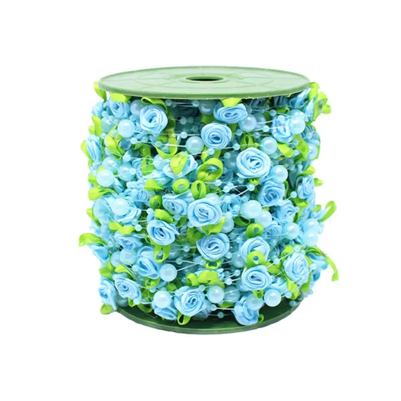 A spool of light blue and green floral ribbon featuring roses, pearls, and leaves.