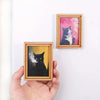 Two framed paintings of cats, one black and white, are displayed against a white background.