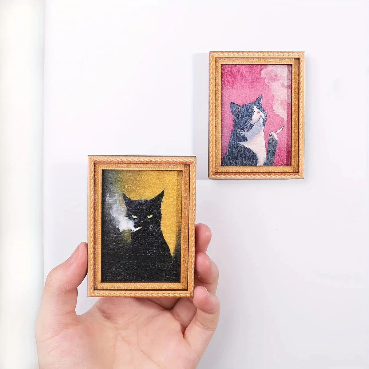 Two framed paintings of cats, one black and white, are displayed against a white background.