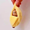 Adorable plush monkey sleeping inside a yellow banana-shaped fabric bag being held by a hand.