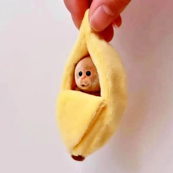 Adorable plush monkey sleeping inside a yellow banana-shaped fabric bag being held by a hand.