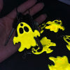A hand holds a set of yellow ghost-shaped reflective keychains against a black background.