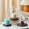 A glass aromatherapy candle holder with a teal candle on a wooden base and dust-proof cover.