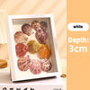 A white shadow box frame displaying various seashells and natural elements.