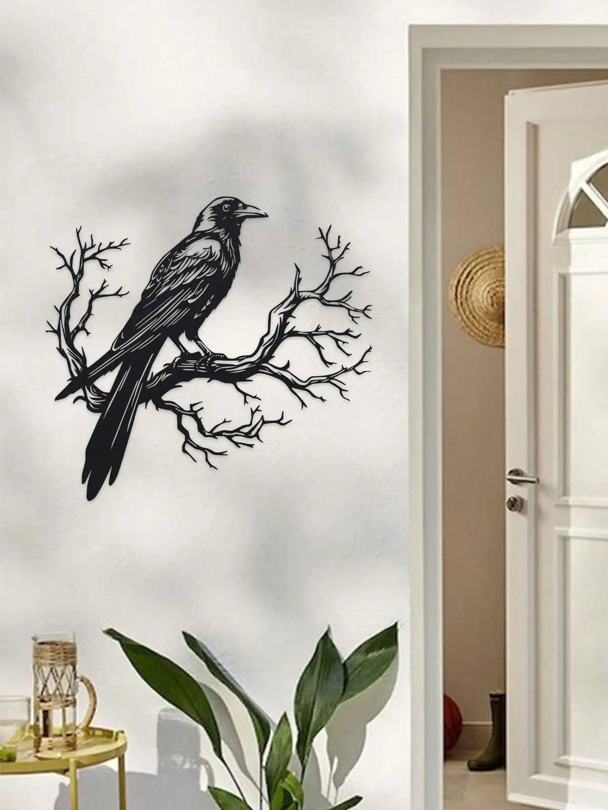 Black raven silhouette on a bare tree branch metal wall art displayed next to a white door frame.
