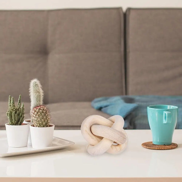 Adorno de nudo tallado en madera, sobre una bandeja blanca junto a una taza verde azulada en una sala de estar moderna.