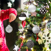 A person hangs various spherical ornaments, including white, black and white polka dot, and silver ones, on a decorated Chris