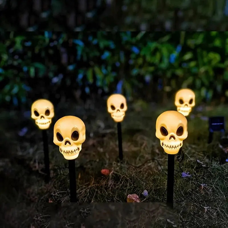 A row of glowing yellow skull lights mounted on black stakes in a dark outdoor setting.