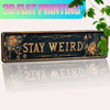 A dark metal wall sign with the text STAY WEIRD surrounded by floral and botanical designs.