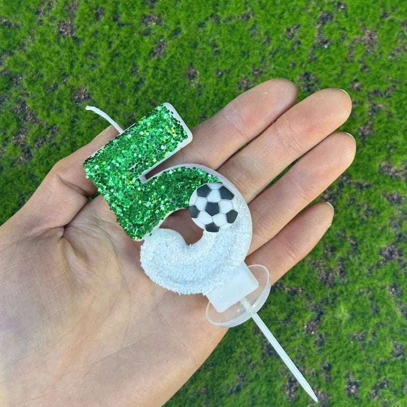 A hand holds a custom number birthday candle shaped like the number 4, covered in green glitter.