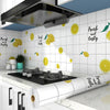 A kitchen wall featuring yellow citrus fruit decals and a black range hood above a countertop.