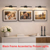 Black frame photo display with picture lights mounted above a wooden cabinet.