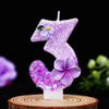 A purple glitter number candle shaped like the number 3 with a flower detail, displayed on a wooden surface.