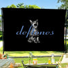 A black banner featuring a stylized cat face and the word Deftones in blue script, set against a green outdoor background.