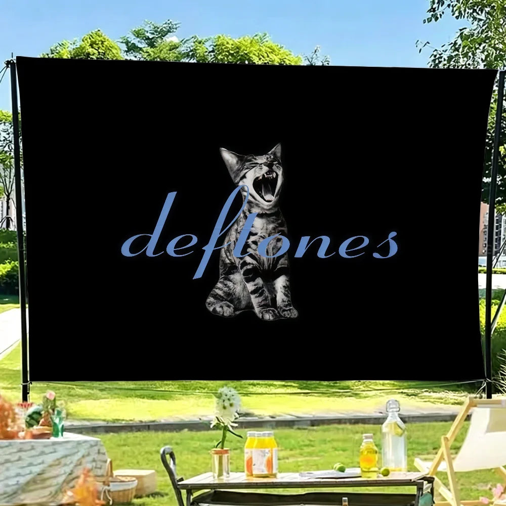A black banner featuring a stylized cat face and the word Deftones in blue script, set against a green outdoor background.