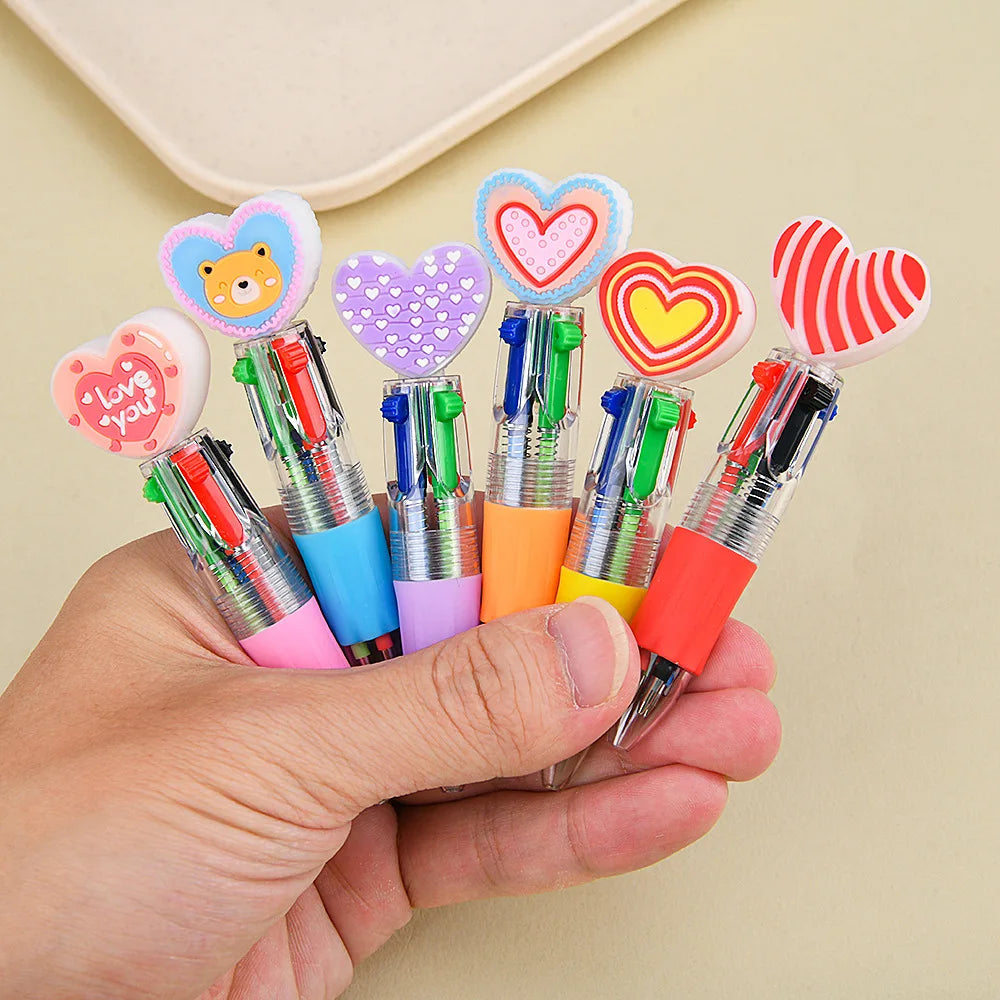 A hand holds a set of heart-shaped multicolor ballpoint pens with decorative tips.