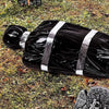 A black plastic bag with silver stripes lying on green grass.