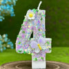 A number cake candle shaped like the number 4 decorated with purple and white flowers and butterflies