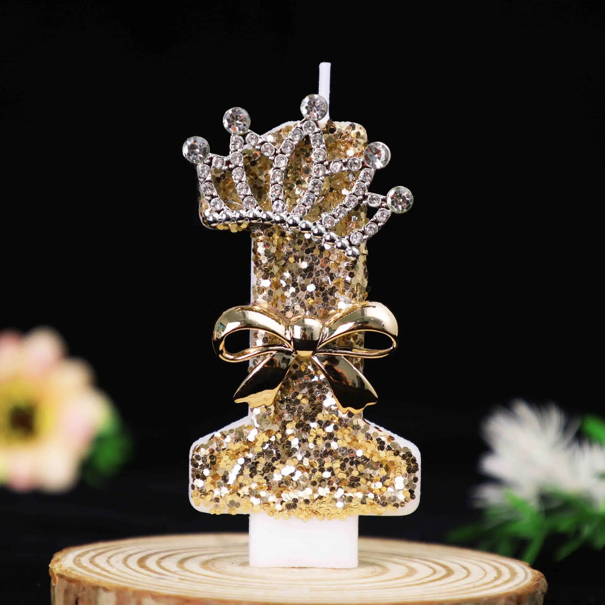 Gold glitter number cake topper candles featuring a rhinestone bow on a wooden stand.