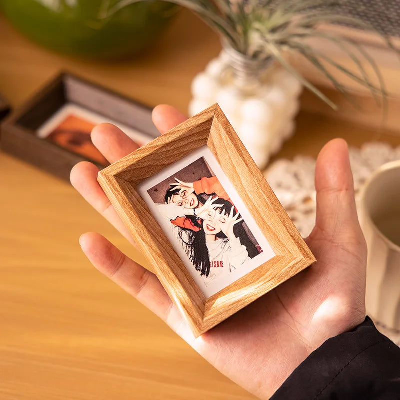 A hand holds a small wooden photo frame containing a vintage-style portrait.