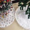 White plush Christmas tree skirt decorated with gold snowflakes and surrounded by green pine branches