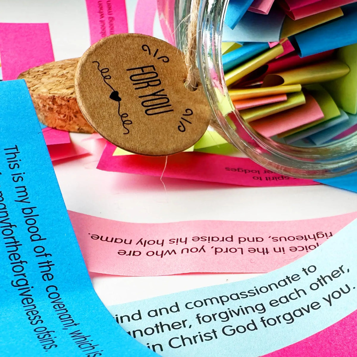 A clear glass jar filled with colorful paper slips, including a tag that reads For You and a pink Bible verse