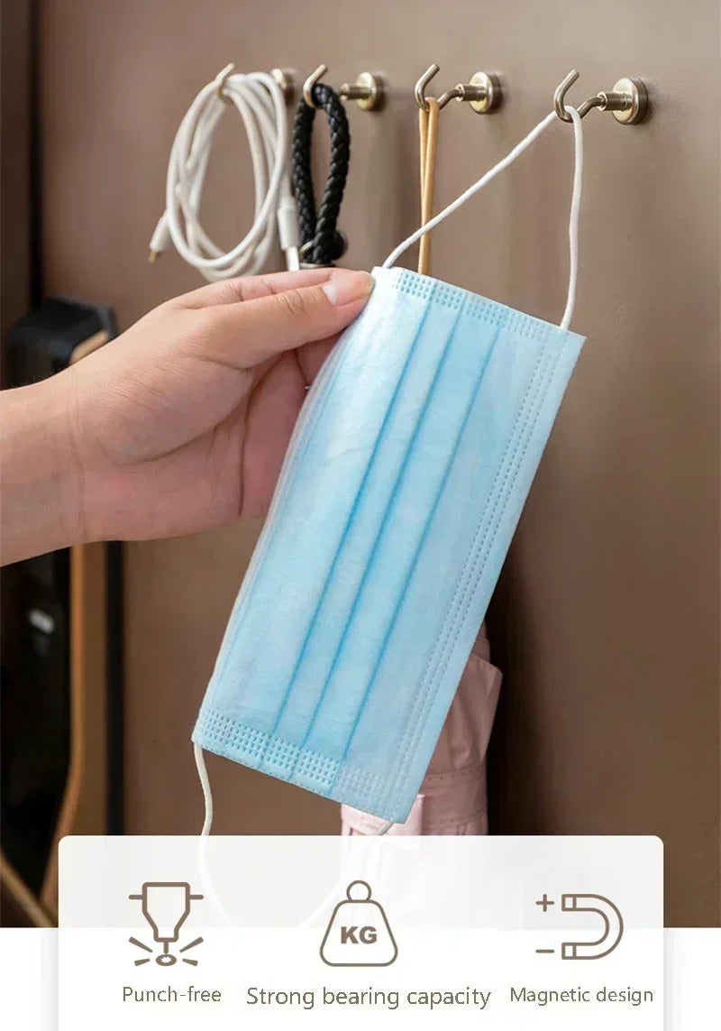 A hand holds a light blue pleated face mask hanging on a wall hook.