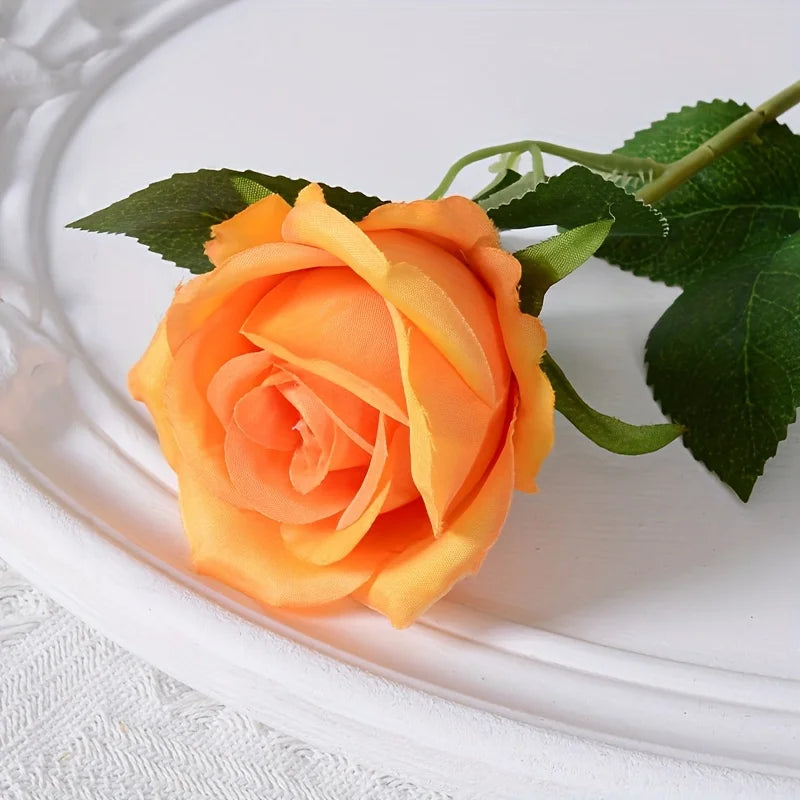 Una rosa artificial de seda naranja con hojas verdes sobre un plato blanco.