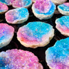 Iridescent blue and pink agate crystal geode pieces scattered on a dark surface.