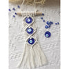 Macrame wall hanging featuring a white cord with multiple blue evil eye pendants.