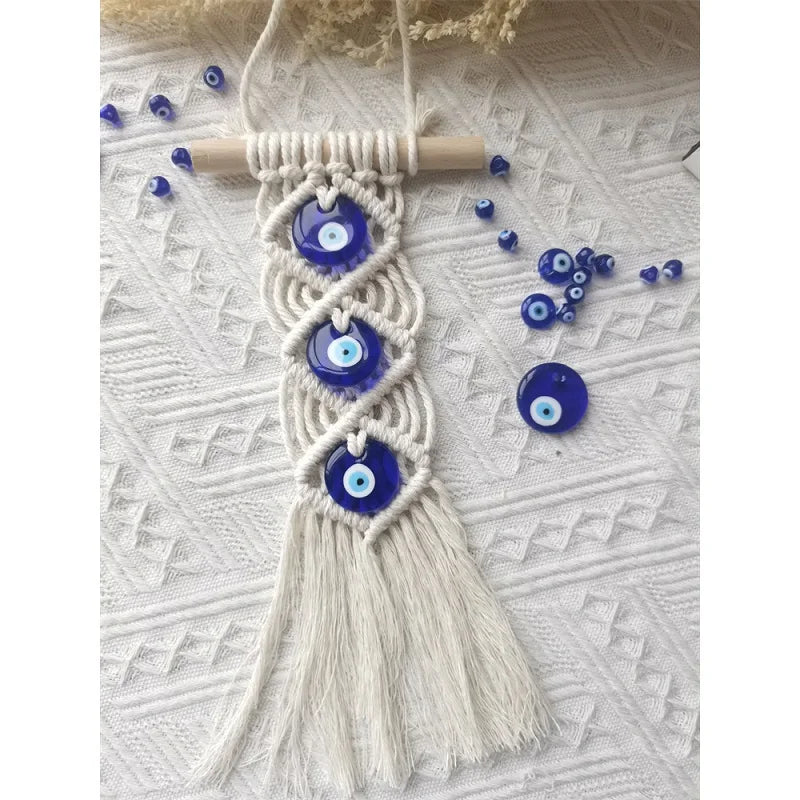 Macrame wall hanging featuring a white cord with multiple blue evil eye pendants.