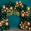 A balloon arch made of metallic gold and dark green balloons against a teal background.