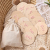 A collection of light wood baby milestone cards with pink lettering arranged on a beige lace fabric next to a linen drawstrin