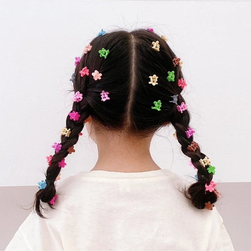 A child's dark hair styled in two braids with colorful flower and star hair claw clips.