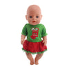 A baby doll wearing a green Christmas outfit with a red skirt and a festive decoration.