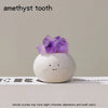 A purple amethyst crystal is placed on a smooth white stone against a neutral background.