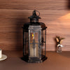 A vintage Nordic iron candle lantern with glass panes sits on a brown surface against a wooden background.