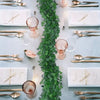 An overhead flat lay of a table setting featuring gold cutlery, glassware, and an artificial ivy garland centerpiece.