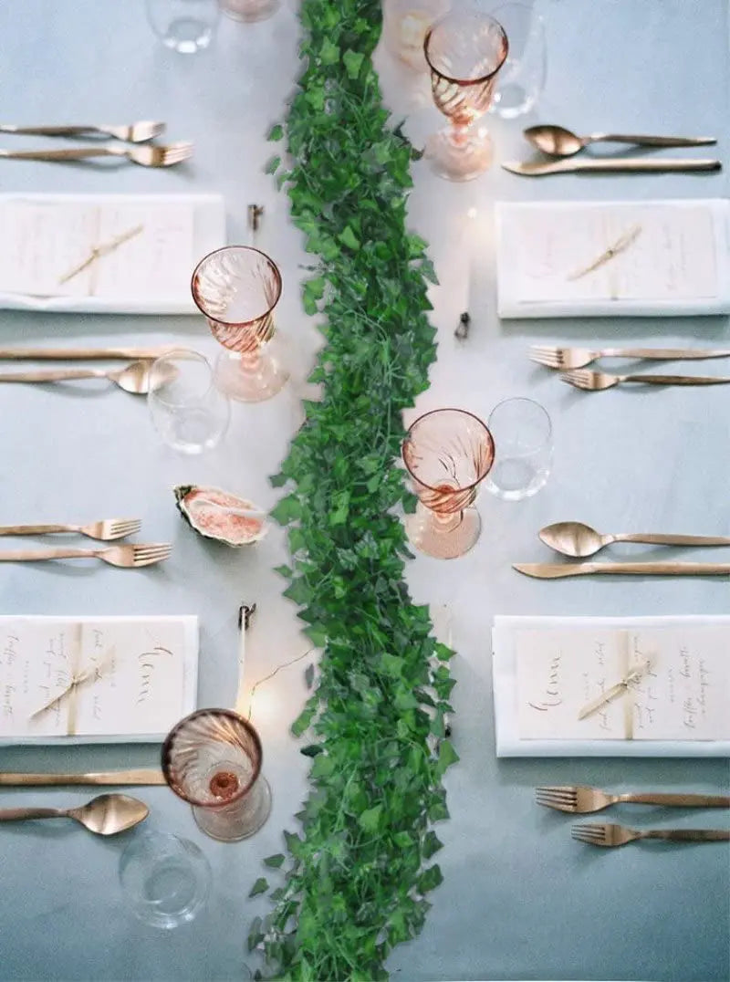An overhead flat lay of a table setting featuring gold cutlery, glassware, and an artificial ivy garland centerpiece.