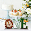 A white cake and cupcakes are displayed next to a wooden jungle animal ornament and letter E.