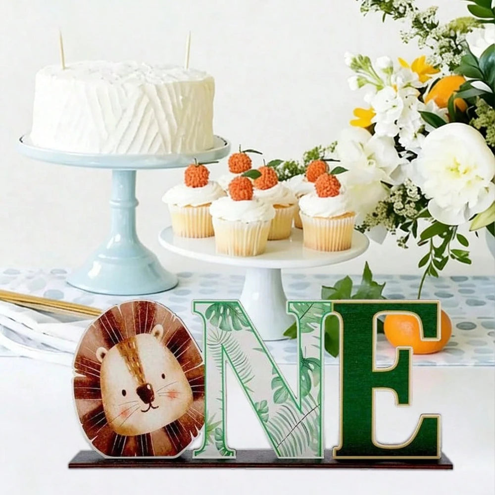 A white cake and cupcakes are displayed next to a wooden jungle animal ornament and letter E.