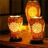 A pair of decorative oil lamps with intricate patterns and warm yellow light sitting on a wooden surface.