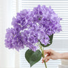 A bouquet of purple artificial hydrangea silk flowers with green leaves.