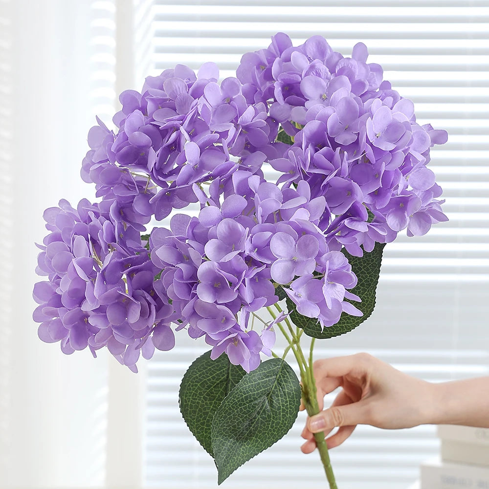 A bouquet of purple artificial hydrangea silk flowers with green leaves.