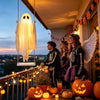 Une décoration fantôme blanche lumineuse pend sur une balustrade de balcon au crépuscule, entourée de décorations d'automne.