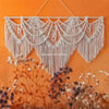 Handwoven boho macrame wall hanging tapestry in cream color against an orange background