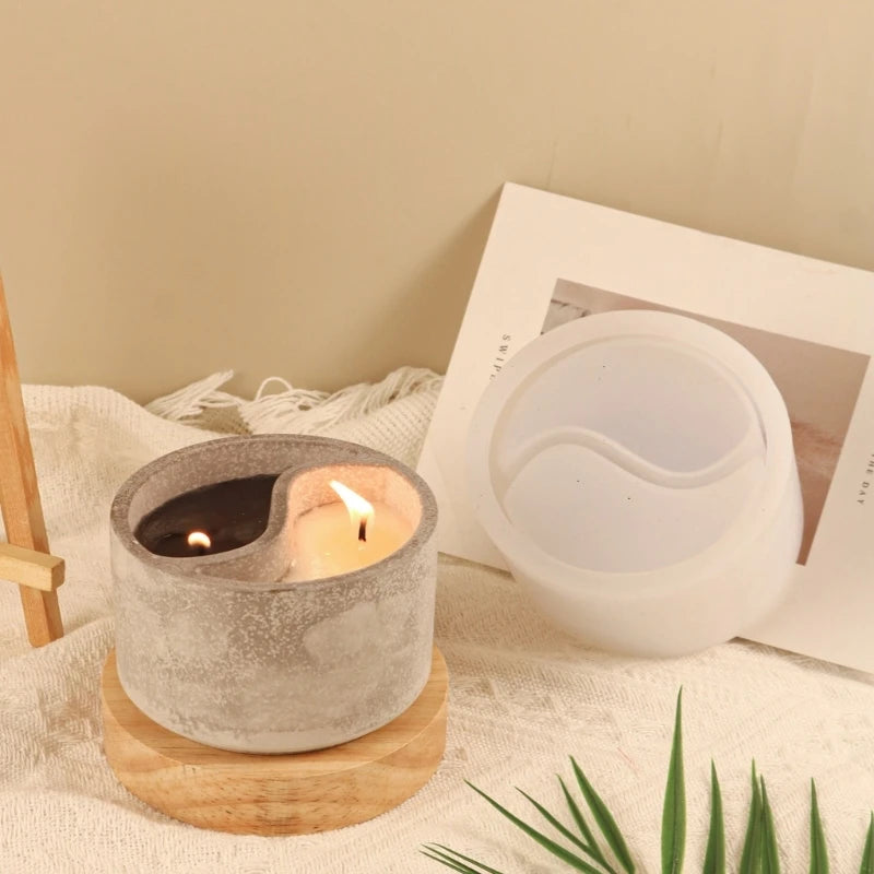 A grey silicone Yin Yang Tai Chi mold used as a candlestick holder sits on a wooden coaster next to a white candle and a fram