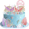 A light blue mermaid cake decorated with pink and gold edible toppers shaped like sea creatures, shells, and seaweed.