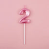 A pink number two candle on a white stick against a light pink background.
